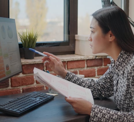 Mulher asiática comparando gráficos em papéis e computador, trabalhando para planejar o projeto de negócios no escritório de inicialização. Funcionário da empresa analisando documentos para projetar dados financeiros e estratégia.