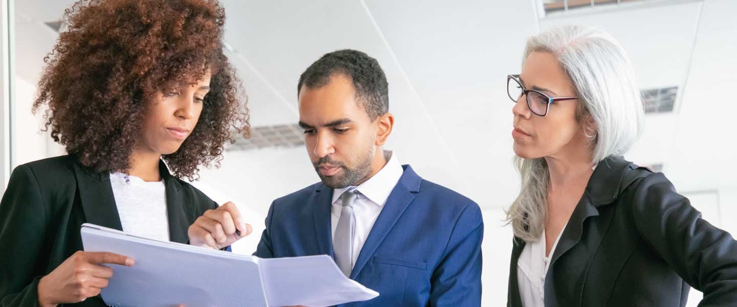 Empregadores de escritório confiantes verificando documentos juntos. Três trabalhadores profissionais focados segurando papéis e assinando relatórios estatísticos na sala de reuniões. Conceito de trabalho em equipe, negócios e gestão